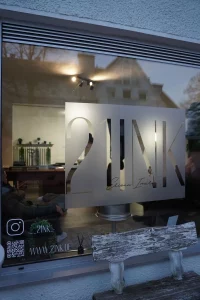 Außenansicht des Tattoo Studios 21NK in Bad Wörishofen mit großem Logo auf dem Schaufenster und Blick ins stilvoll eingerichtete Studio.